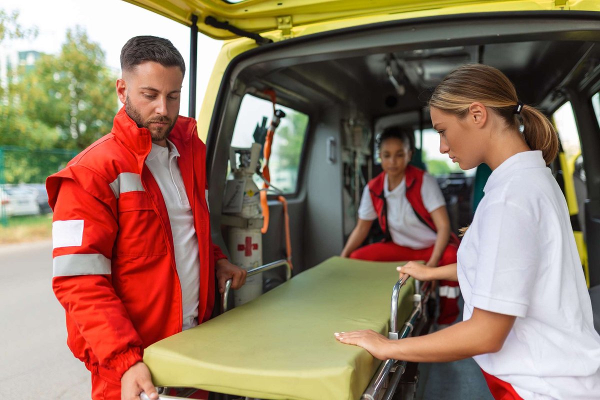 Emergency medical workers carefully unload a stretcher from an ambulance, preparing to assist a patient during a routine emergency response.