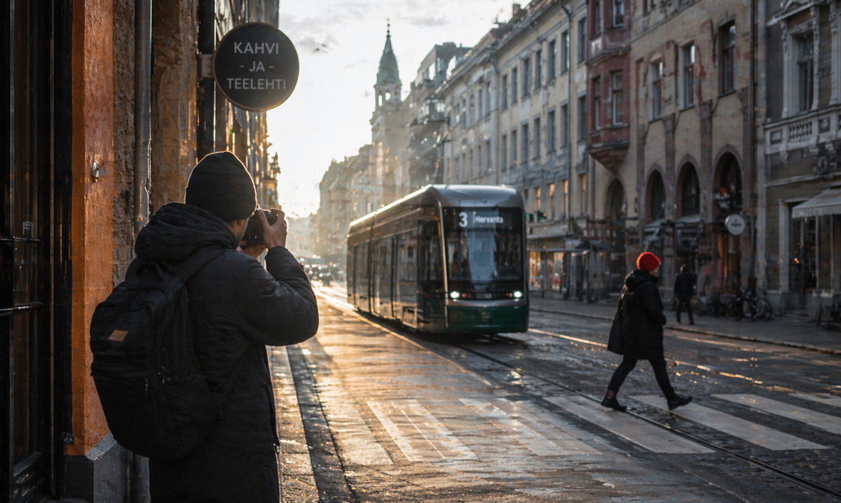 A photographer captures a quiet urban scene as a tram passes and a lone pedestrian crosses the street in soft golden light.
